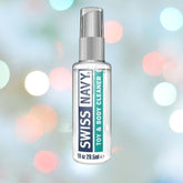 A clear bottle of Swiss Navy Toy and Body Cleaner, featuring information about its silicone lubricant-friendly formula, is positioned against a colorful, softly blurred background.
